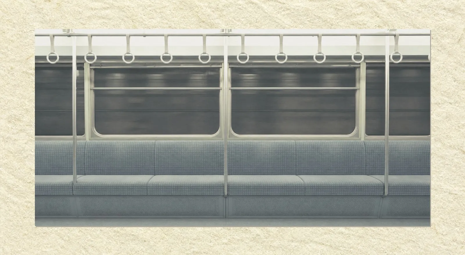 The inside of an empty commuter train carriage seen square-on from the aisle. A row of empty bench seats runs the width of the frame with hand straps hanging motionless in a line above them. Through the windows there is only the black of a tunnel wall. Nobody is present.