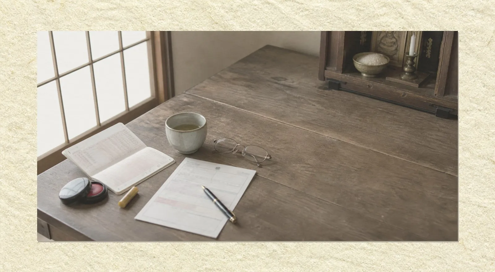 A low wooden table in an old Japanese house, seen slightly from above. On it are an open bank passbook, a personal seal beside a small red ink pad, a partly filled form with a fountain pen laid across it, folded reading glasses and a cup of tea gone cold. At the right edge stands the lower corner of a household Buddhist altar with an unlit candle and a small bowl of rice. Nobody is present.